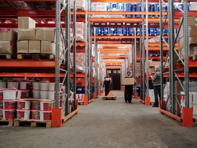 Warehouse interior showing workers handling boxes and organized shelves filled with products.
