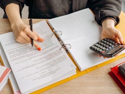 A woman reviewing documents and using a calculator on a wooden table.